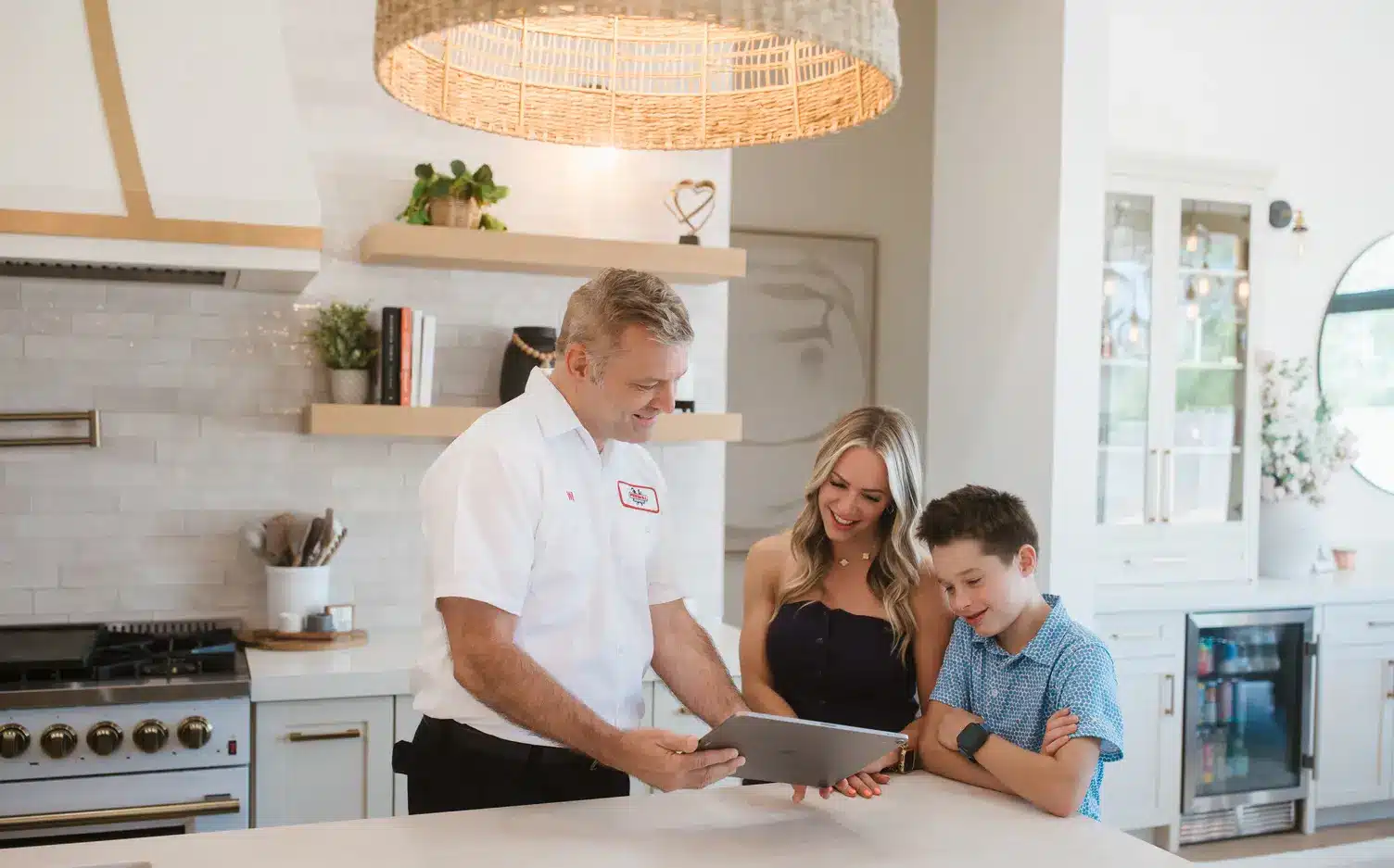 ProSkill technician reviewing service specials on a tablet with a homeowner and her son in their kitchen